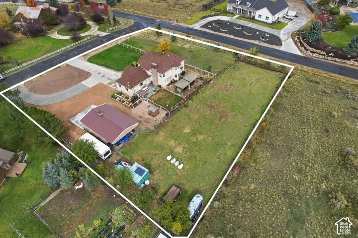 Aerial perspective of a sprawling lot featuring a multi-story residence, a detached secondary structure with metal roofing, an expansive lawn, and concrete driveway paving