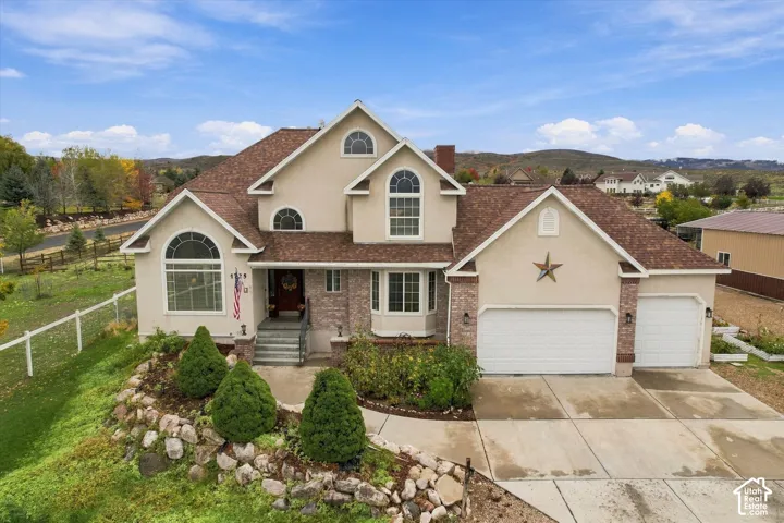 Stucco exterior with multi-textured stone veneer accents, multi-gabled roofline, arched window detailing, three-car garage, and terraced stone retaining walls