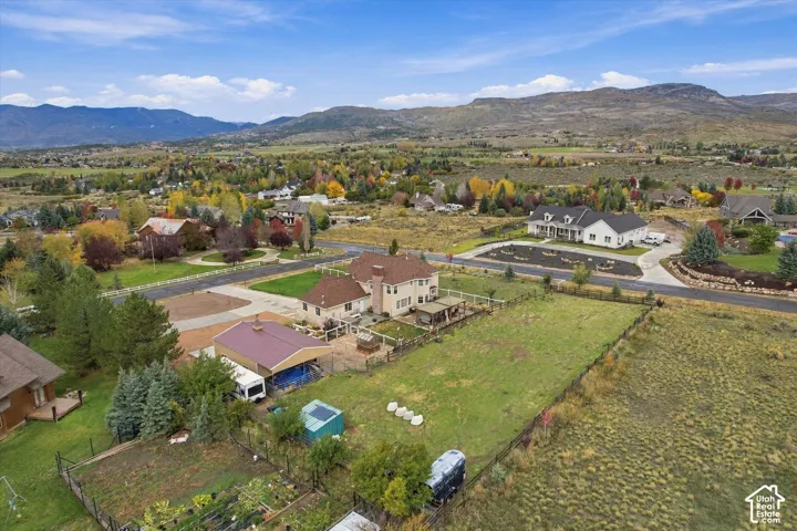 Aerial perspective featuring an expansive lot, a detached metal-roofed outbuilding, fenced perimeter, and mountainous horizon