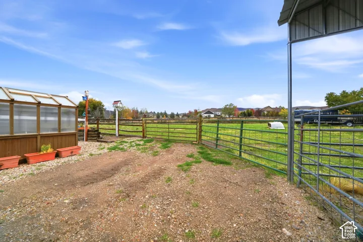 Outdoor area featuring a greenhouse, metal livestock fencing, a gravel yard, and a covered metal structure