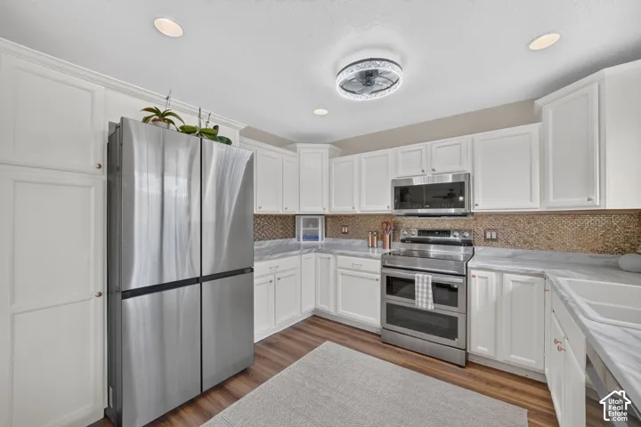 Kitchen featuring white cabinetry, stainless steel appliances, marble-patterned countertops, mosaic tile backsplash, and wood-finish flooring