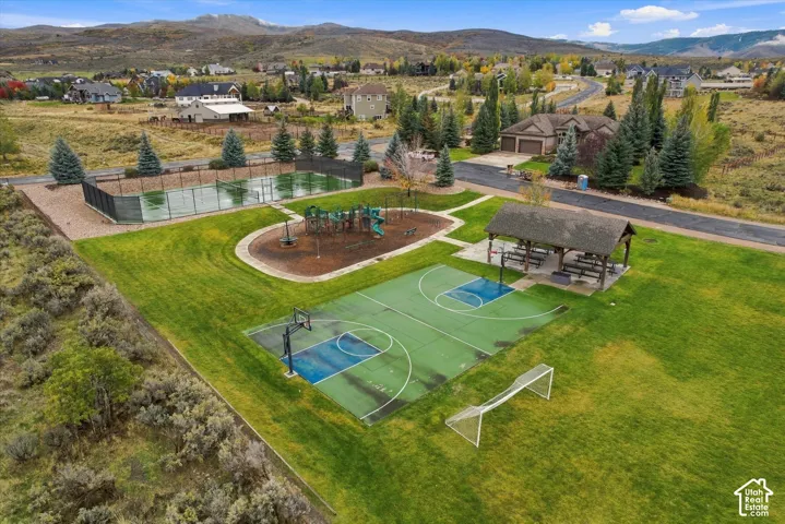 Recreational park featuring a fenced tennis court, basketball court with soccer goal, playground area, and a covered pavilion