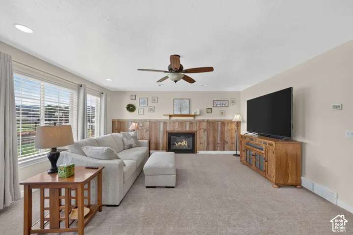 Living area featuring a fireplace with a wood-plank accent wall, recessed lighting, ceiling fan, and large windows