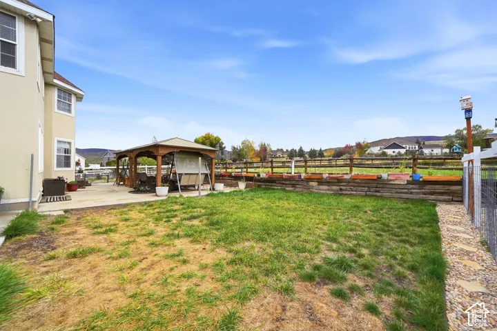 Fenced backyard featuring a covered wood-frame gazebo, concrete patio, tiered timber retaining wall, and mountain backdrop