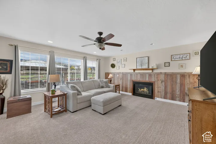 Living area featuring a fireplace with a wood-plank accent wall and floating mantel, recessed lighting, ceiling fan, and large windows with integrated grids