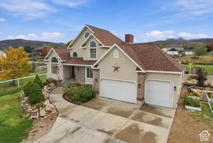 Stucco and brick exterior featuring an attached three-car garage, steep-pitch shingle roof, arched windows, and professional rock-accented landscaping