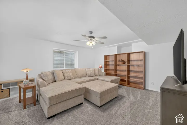 Neutral-toned carpeting, wood-finish built-in shelving, and a ceiling fan with integrated lighting