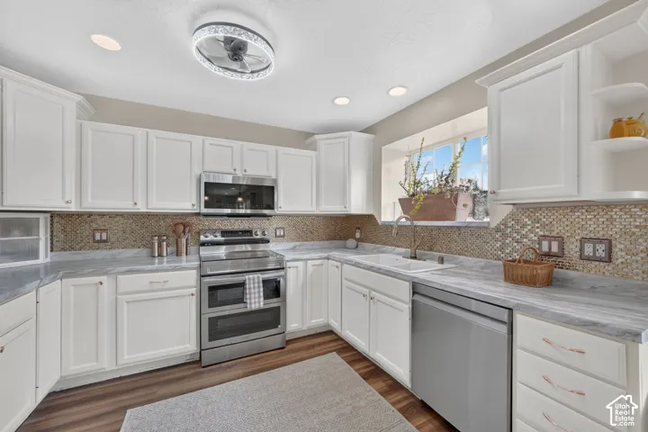 Kitchen featuring white shaker-style cabinetry, stainless steel appliances, patterned stone-finish countertops, mosaic tile backsplash, and wood-finish flooring
