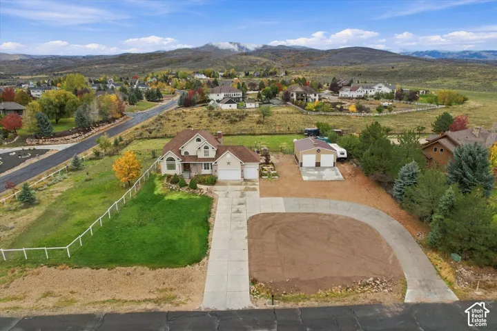 Multi-level residence featuring a multi-car attached garage, detached workshop, expansive concrete driveway, white post-and-rail fencing, and mountain scenery