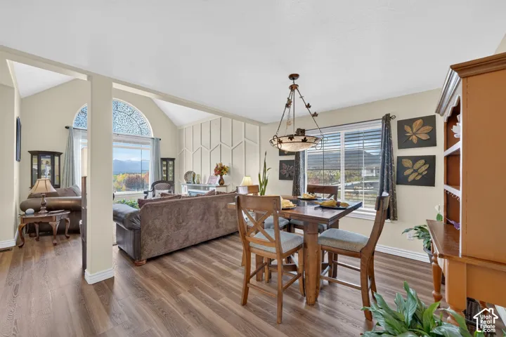 Open living area featuring vaulted ceilings, wood-finish flooring, a decorative wall panel accent, a multi-light chandelier, and an arched window