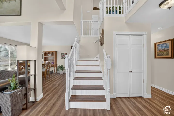 Foyer featuring wood-finish flooring, a staircase with white balusters and wood-tone treads, high ceilings, and a double-door closet with millwork trim