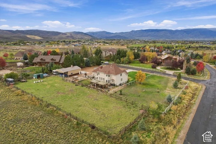 Aerial perspective of property featuring a multi-story residence, a detached garage, expansive fenced grounds, and mountain range backdrop