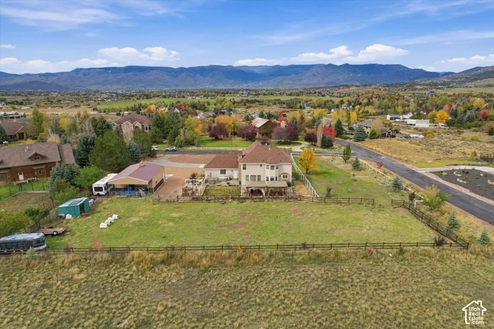 Aerial perspective featuring expansive acreage, a multi-car detached garage, fenced perimeter, and a mountain range backdrop