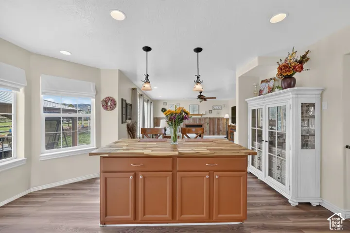 Kitchen featuring a center island with a wood countertop, dual overhead pendant lighting, recessed ceiling lights, wood-finish flooring, and built-in cabinetry with glass-paneled doors