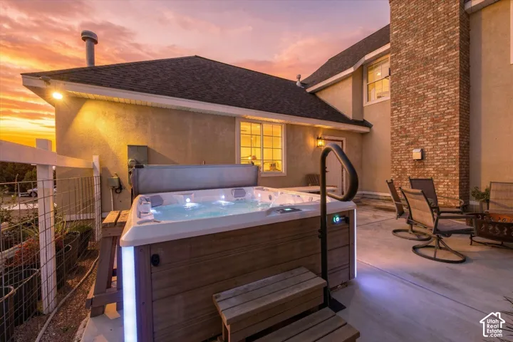 Concrete patio featuring an integrated hot tub with exterior lighting, an attached handrail, and a brick chimney exterior
