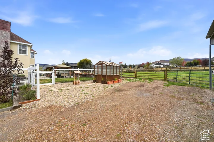 Expansive outdoor area featuring a wood-frame greenhouse, gravel ground cover, split-rail fencing, and metal perimeter enclosure