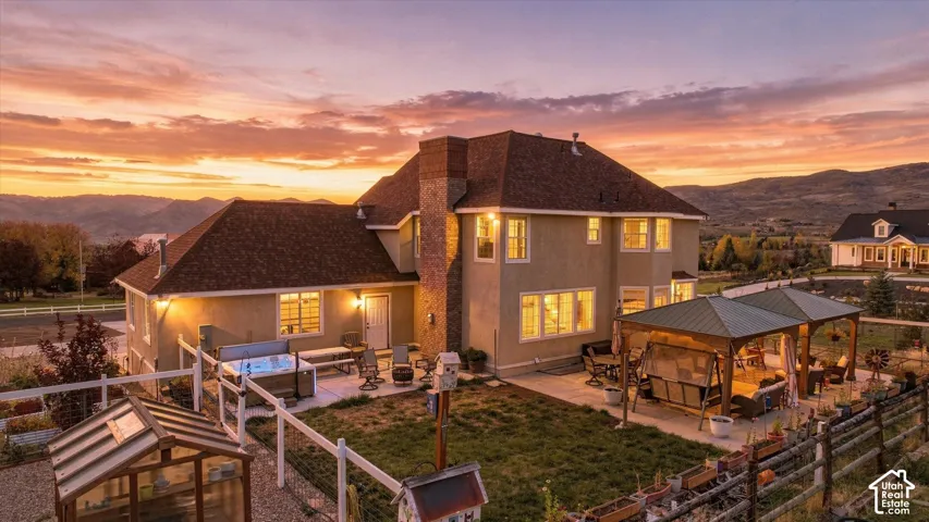 Stucco exterior residence featuring an external stone chimney, rear patio with metal-roofed gazebo, built-in hot tub, and detached greenhouse