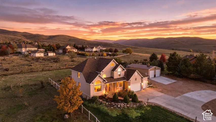 Multi-level residence with stucco exterior, steep pitched rooflines, detached secondary garage, extensive concrete driveway, and natural stone landscaping elements