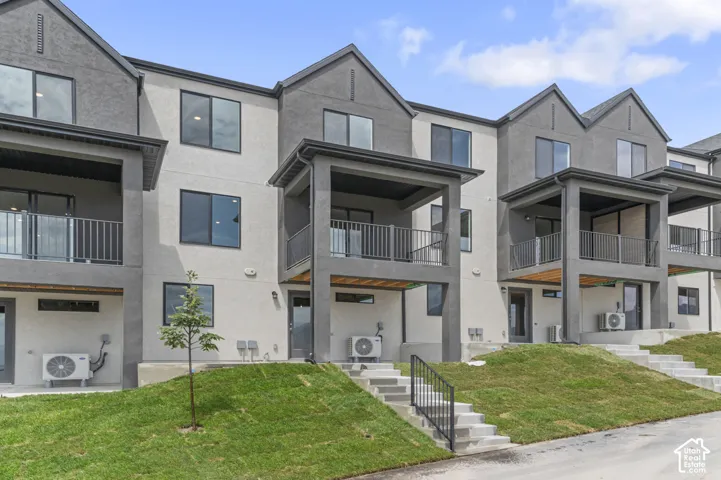 Multi-story structure featuring a stucco exterior with gabled rooflines, covered balconies with metal railings, and concrete staircases with metal handrails