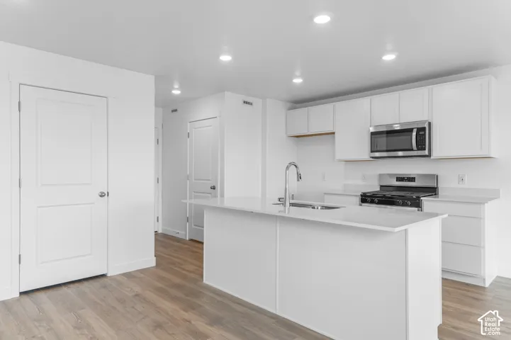 Kitchen featuring white cabinetry, an island with a light-toned countertop, wood-finish flooring, stainless steel appliances, and recessed lighting