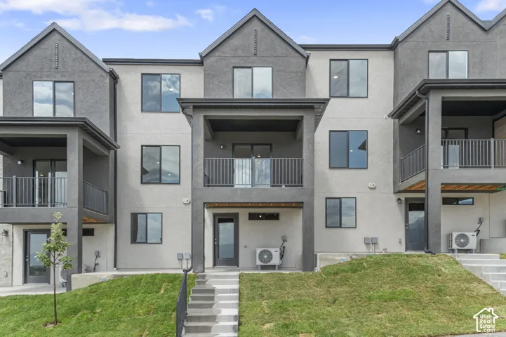 Multi-story exterior featuring a stucco facade, covered balconies with metal railings, concrete stairs, and paved lower-level entries