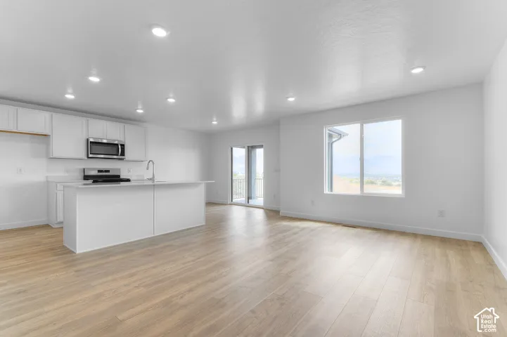 Open-concept interior featuring wood-finish flooring, recessed lighting, and a kitchen equipped with white cabinetry, a center island, and stainless steel built-in appliances