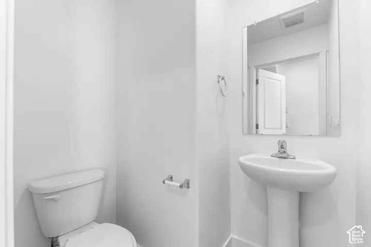 Pedestal sink with a single-handle chrome faucet, rectangular wall-mounted mirror, and standard-height toilet