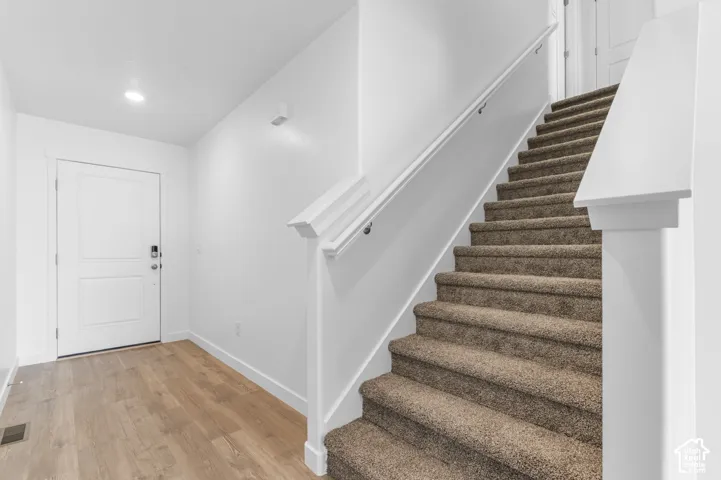 Entryway featuring wood-finish flooring, a white paneled front door, and a staircase with carpeted treads and a white wooden handrail