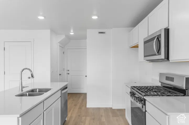 Kitchen featuring white cabinetry, quartz countertops, wood-finish flooring, recessed lighting, and stainless steel appliances