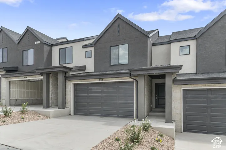 Contemporary townhome exterior featuring a multi-toned stucco facade, dual-pitched rooflines, stone masonry accents, a concrete driveway, and integrated garage doors