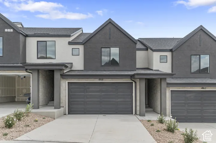 Contemporary multi-level exterior featuring a combination of stucco and stone siding, dark-toned garage door, asphalt shingle roofing, and recessed covered entryways