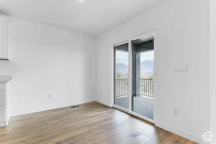 Wood-finish flooring, white walls, and sliding glass doors opening to a covered deck featuring metal railings and mountain scenery