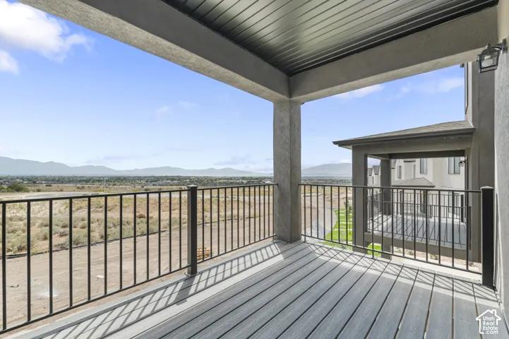 Covered balcony featuring composite decking, black metal railings, a dark paneled ceiling, and mountain backdrop