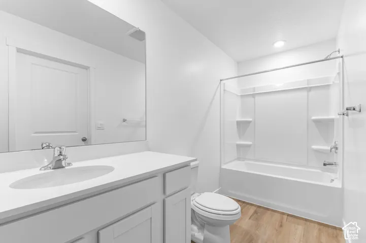 Bathroom featuring a white vanity with an integrated basin, a large wall-mounted mirror, a tub and shower combination with integrated shelving, and wood-finish flooring