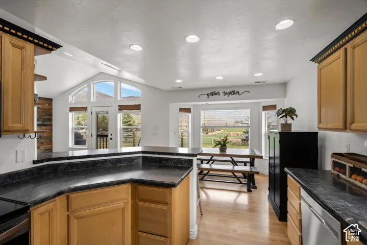 Kitchen featuring warm-tone wooden cabinetry, dark stone-finish countertops, recessed lighting, and a vaulted ceiling with oversized windows