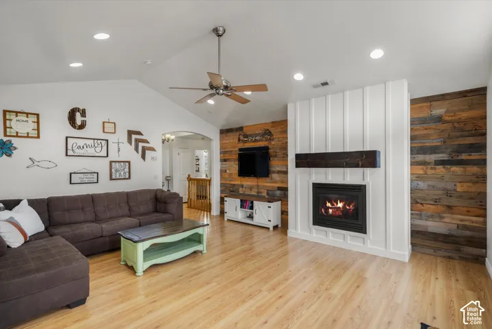 Vaulted ceilings featuring a central fan, fireplace with a dark wood mantel, board-and-batten detailing, wood-finish flooring, and reclaimed-style wood paneling accent walls