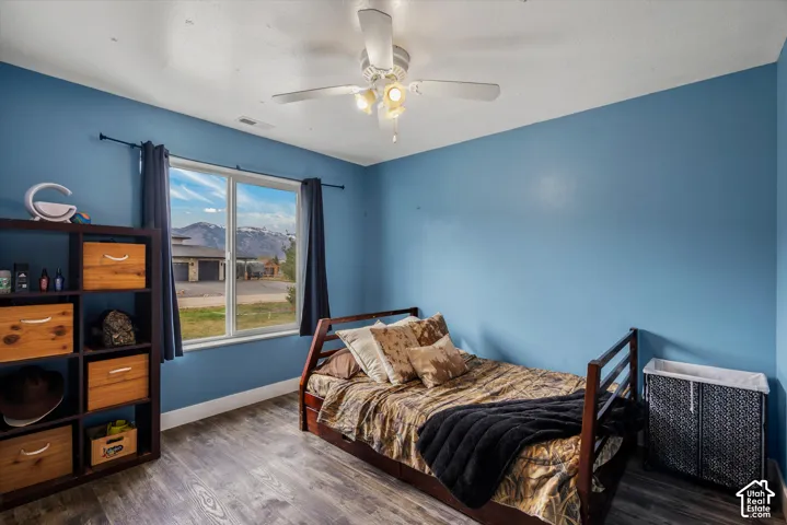 Bedroom featuring wood-finish flooring, a ceiling fan with integrated lighting, and a large window with mountain scenery