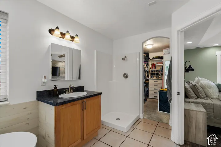 Bathroom featuring a wood-finish vanity with a dark-toned countertop, integrated mirror cabinetry, a shower stall with a white surround, and tile flooring