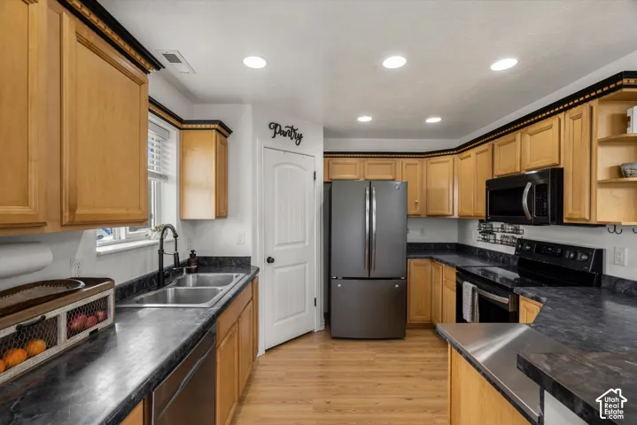 Kitchen featuring natural wood cabinetry, dark-tone countertops, stainless steel appliances, dual-basin stainless steel sink with a matte black faucet, and pantry with a paneled door