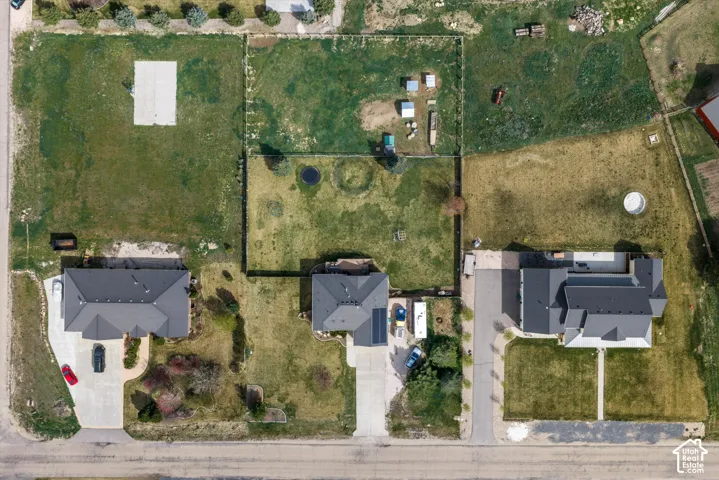 Aerial view of a residential lot featuring expansive acreage, a fenced perimeter, a concrete driveway, and an attached solar panel system
