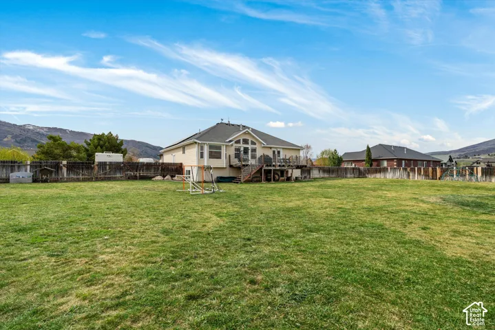 Expansive backyard featuring a large grass lawn, a wood deck with stairs, a perimeter wood fence, and mountain scenery