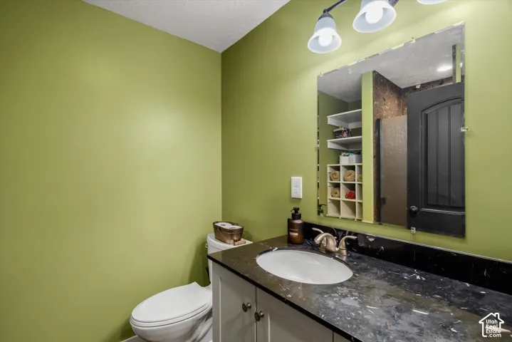 Vanity featuring a dark stone-finish countertop, white oval undermount sink, metallic faucet, and white cabinetry, complemented by a large wall-mounted mirror, three-light fixture, and built-in shelving