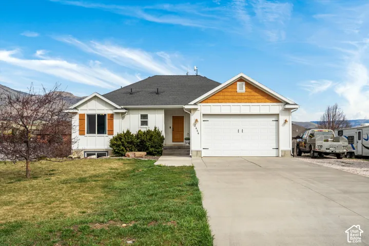 Single-level residence featuring vertical board-and-batten siding, decorative gable shingles, a paved concrete driveway, an attached two-car garage, and a backdrop of mountain scenery