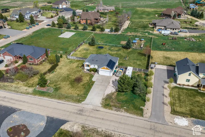 Aerial perspective of a residential property featuring an attached two-car garage, roof-mounted solar panels, concrete driveway, and a fenced-in backyard area
