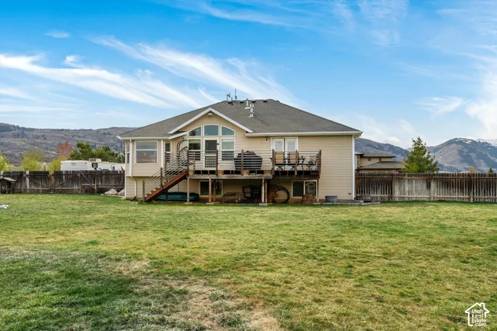 Expansive backyard featuring a large grass lawn, a raised wooden deck with metal railings, a full-height arched window, and a mountain backdrop