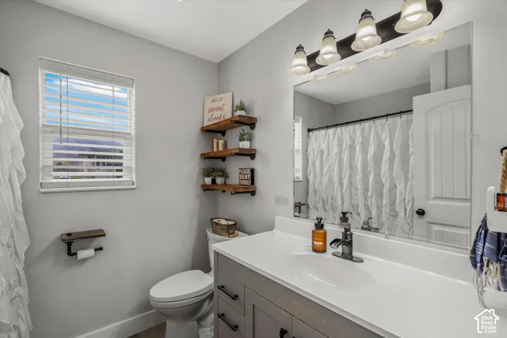 Bathroom vanity with a white countertop, industrial-style wall-mounted shelving, large rectangular mirror, and multi-bulb vanity light fixture