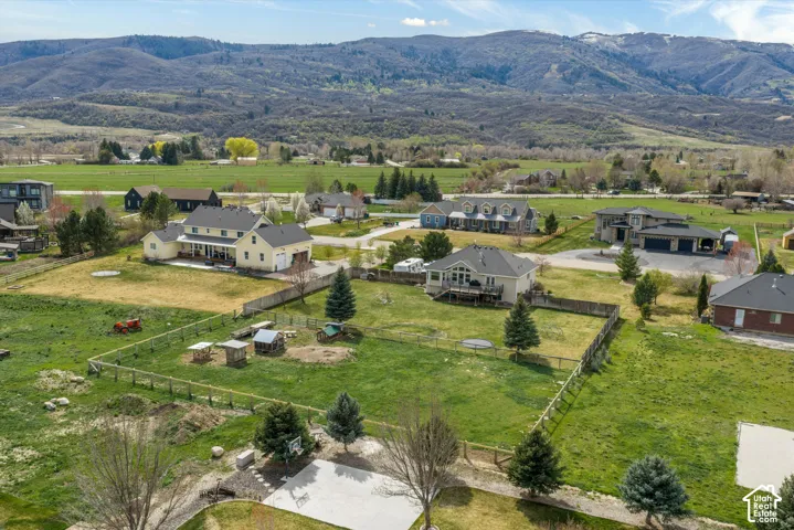 Aerial perspective featuring a multi-acre lot with perimeter fencing, a concrete pad, mature evergreen trees, and expansive mountain scenery