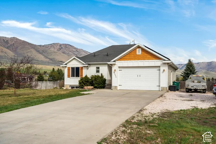 Single-story residence featuring white board-and-batten siding, contrasting wood-tone gables and shutters, a two-car garage, and concrete driveway, set against a prominent mountain backdrop