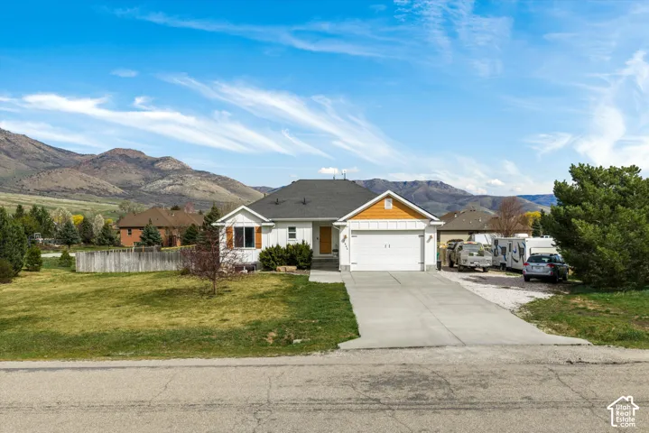 Single-story residence featuring a multi-material facade with wood-style siding accents, a two-car garage, concrete driveway, and mountain backdrop