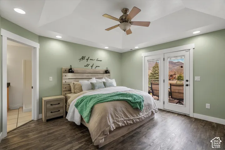 Tray ceiling with integrated recessed lighting, wood-finish flooring, ceiling fan with light fixture, and glass-paneled double doors featuring mountain scenery
